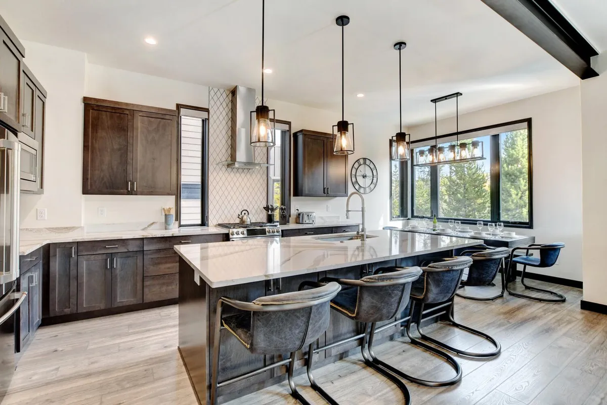 A spacious kitchen with a large island countertop, surrounded by bar stools and bathed in natural light from expansive windows. The kitchen is equipped with modern, high-end appliances and provides ample space for cooking and socializing. The arrangement invites family and friends to gather around for casual meals or festive preparations.