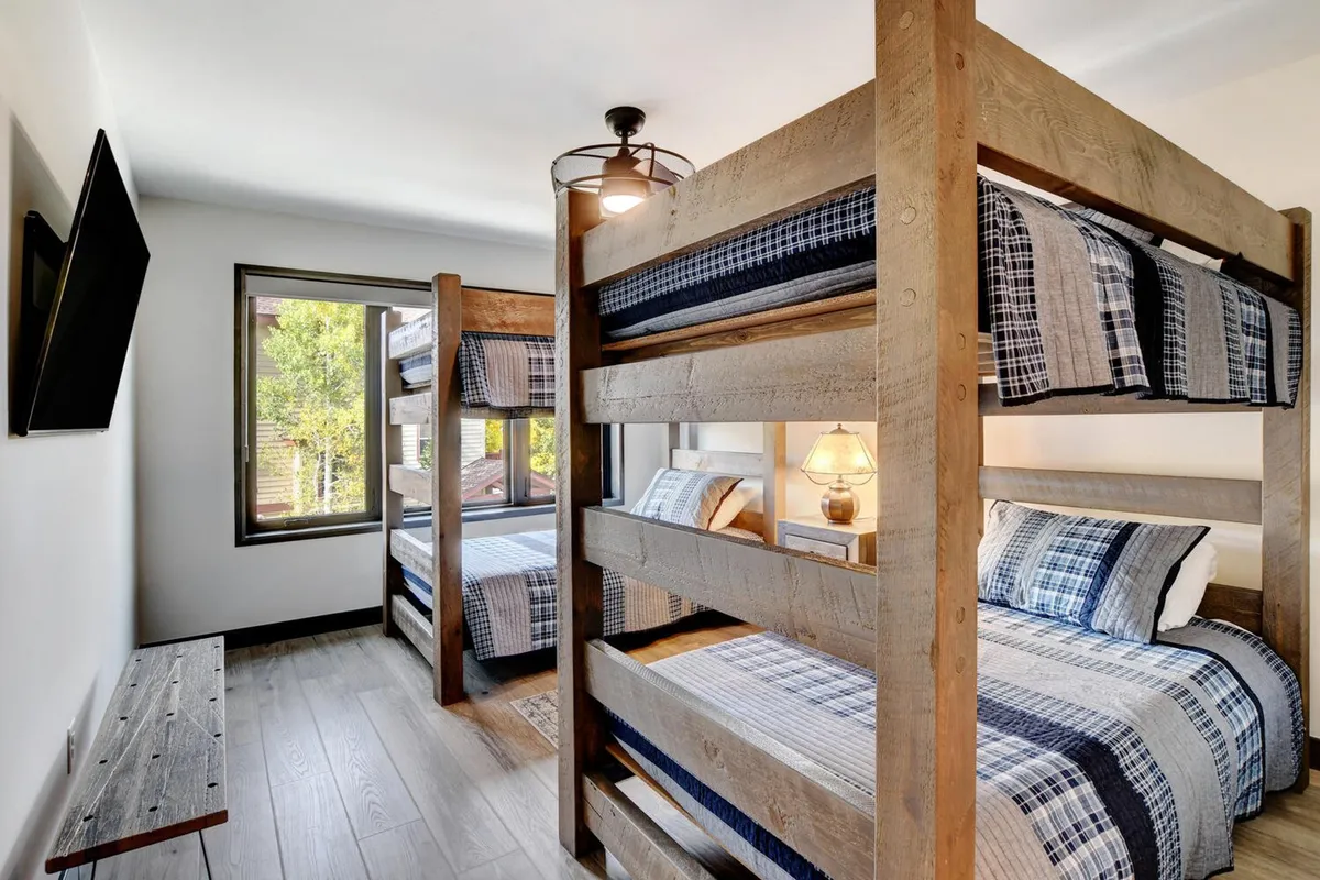 A cozy bunk room with built-in bunk beds, soft lighting, windows, a lamp, and a television. The arrangement is ideal for families or groups, offering a playful and comfortable environment for young guests or multiple friends.