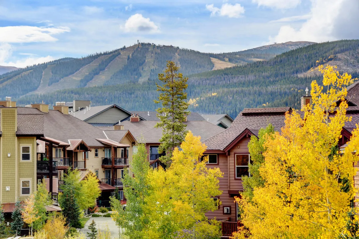 An exterior view of the property surrounded by a vibrant display of colorful autumn trees and set against a majestic mountain backdrop. The architectural details of the buildings blend harmoniously with the natural setting, suggesting opportunities for hiking, nature walks, and photography.