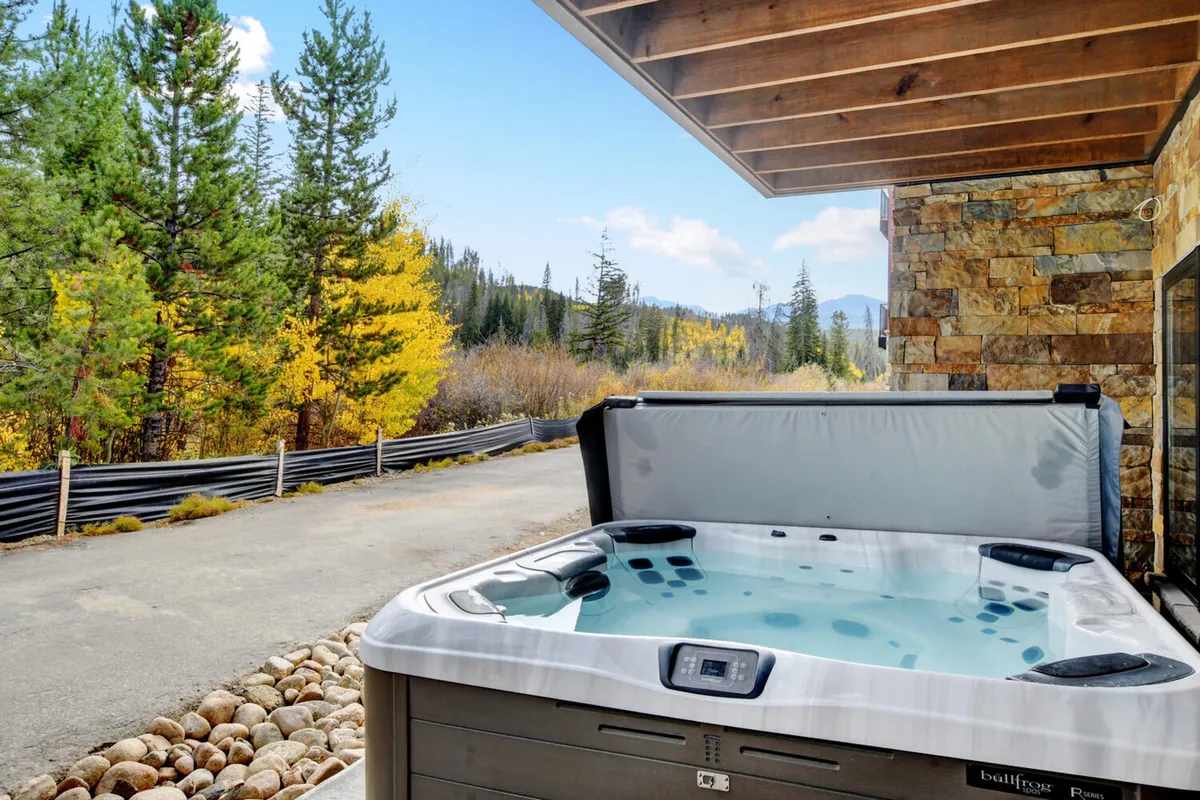 This exterior image features a private outdoor hot tub surrounded by lush trees, set against a backdrop of mountain views. The tranquil mood is accentuated by the inviting water, perfect for relaxing under the stars or after a day of adventure.