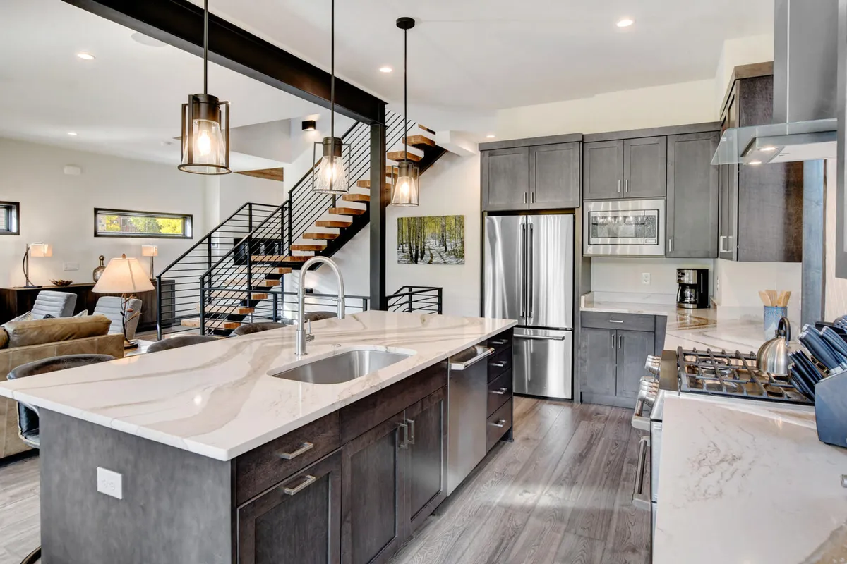 A sleek, modern kitchen with a prominent island at the center, surrounded by stainless steel appliances and illuminated by stylish pendant lighting. The open layout makes it ideal for cooking together or hosting family celebrations, and the cozy ambiance encourages lingering conversations and shared experiences.