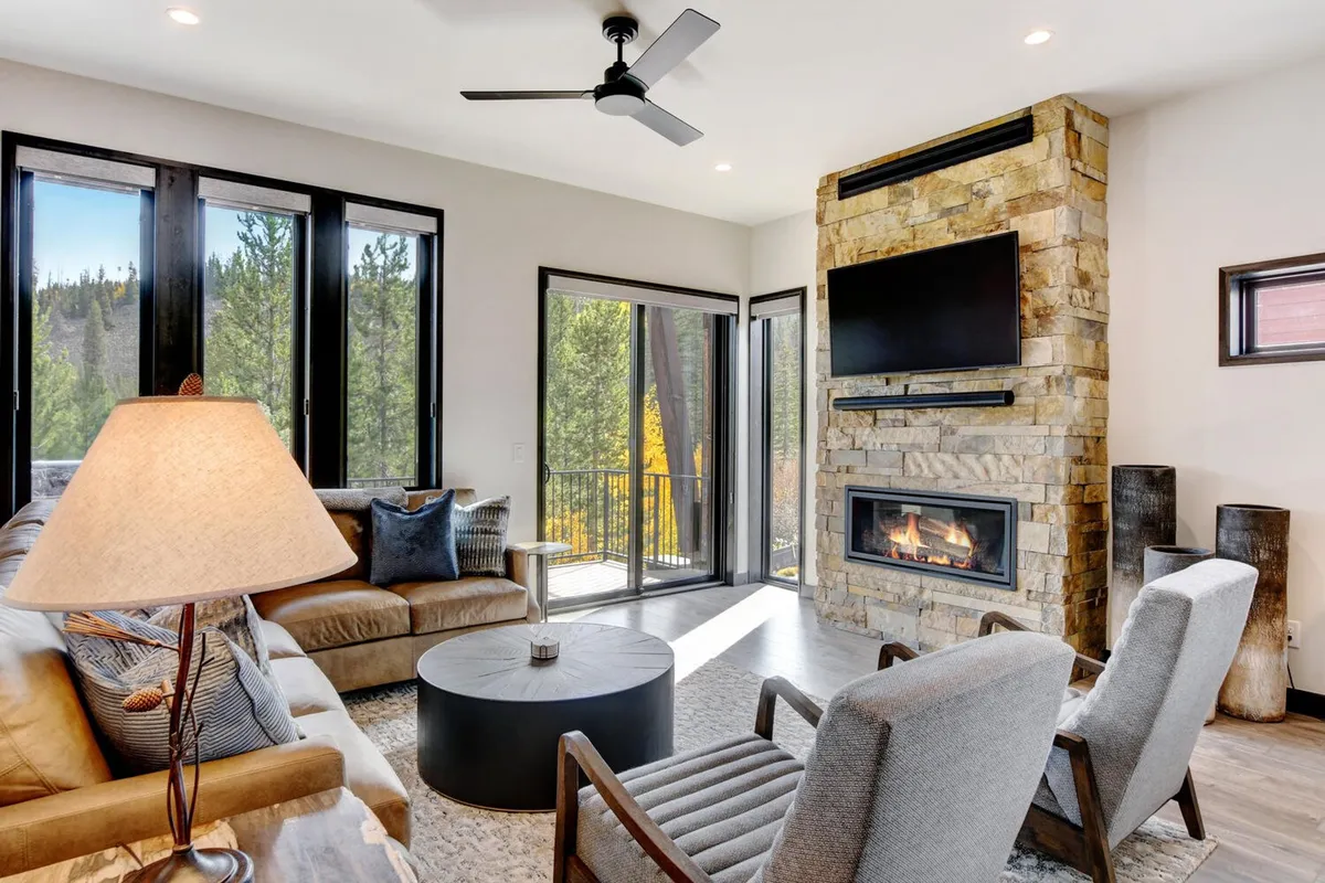 A cozy living room with a plush sofa, elegant coffee table, a modern fireplace as a focal point, and expansive windows offering views of the sunset over the mountains. The space is perfect for relaxing, socializing, and unwinding by the fire.