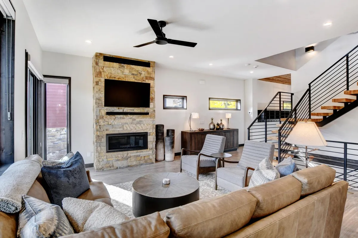 A contemporary living area centered on a striking stone gas fireplace, complemented by comfortable seating and a modern TV unit. The mood is cozy and ideal for sipping coffee or enjoying quiet conversation by the fire.
