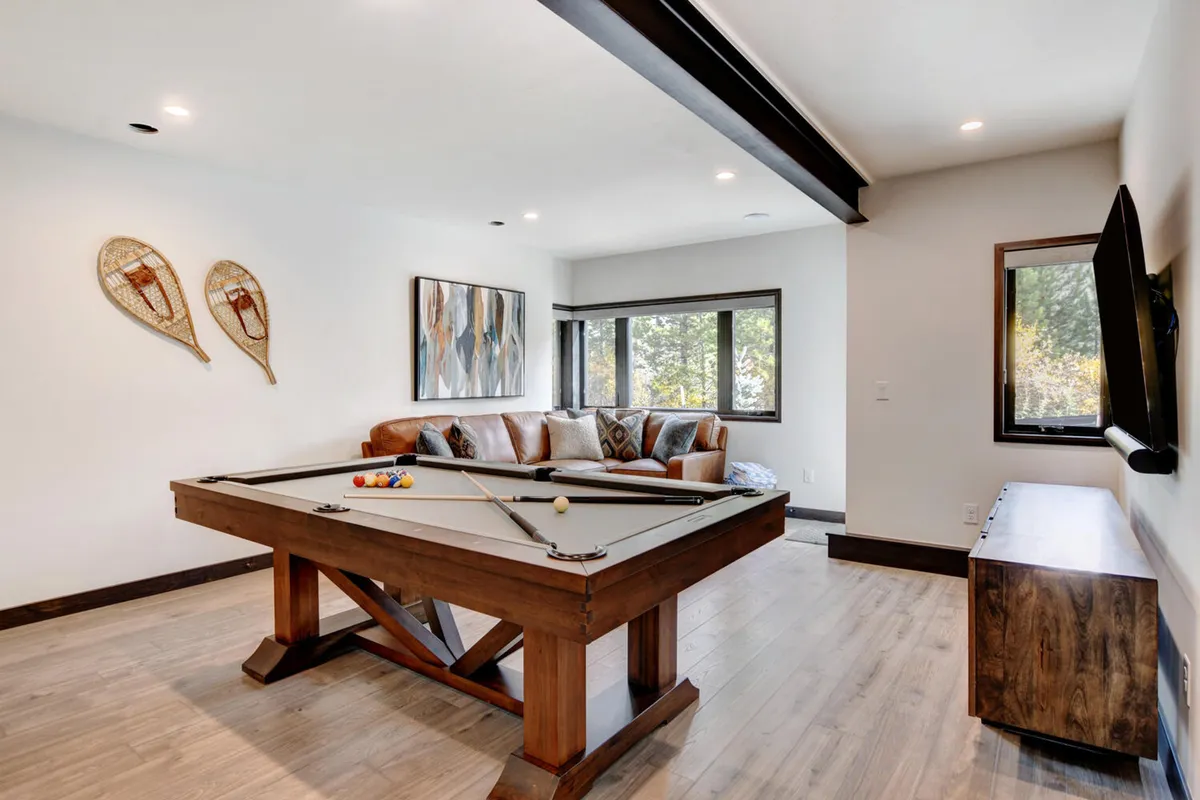 A vibrant and inviting game area featuring a pool table, comfortable sofa, tasteful artwork, and generous windows that allow natural light to flood the room. The space is set up for fun and socializing, perfect for hosting game nights and creating lasting memories.